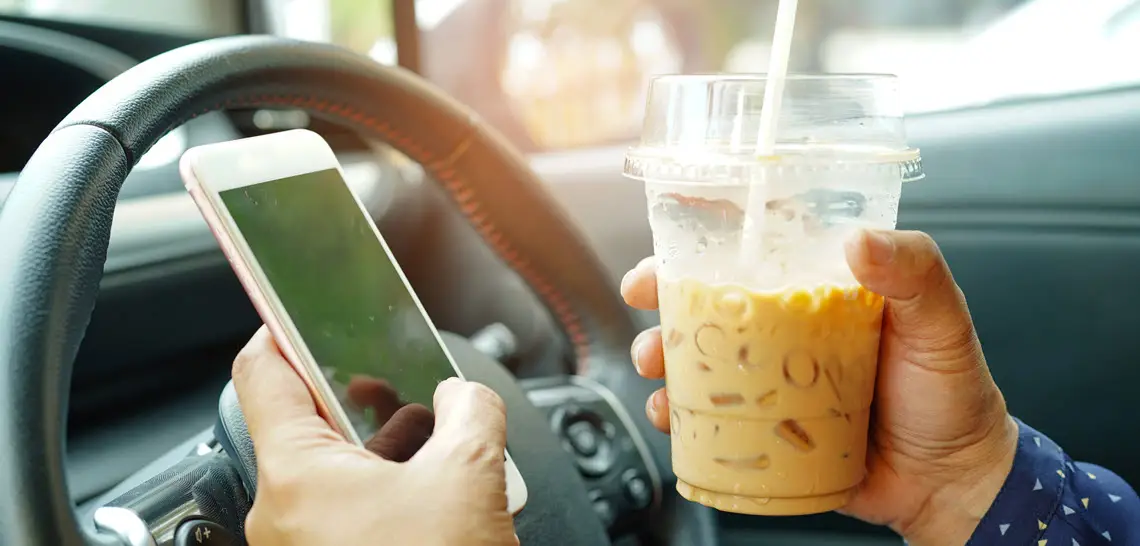 Distracted driver texting and holding coffee